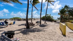 Ein Strand mit Palmen, einer Holzbank und einem Grill.