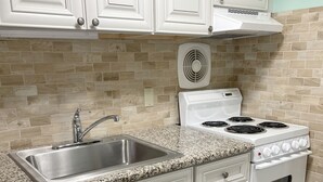 A kitchen with white cabinets, a granite countertop, a stainless steel sink, a white stove, and a wall-mounted fan. - 1BR Condo Beach Block Location – Under 500 feet to the Beach & Boardwalk (Ocean City)