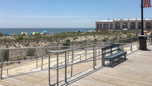 A wooden boardwalk with a bench, a fence, and beach umbrellas. - 1BR Condo Beach Block Location – Under 500 feet to the Beach & Boardwalk (Ocean City)