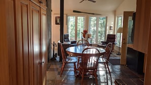 A dining area with a round table and chairs, a ceiling fan, and large windows. - Treehouse on the river. (Au Train)