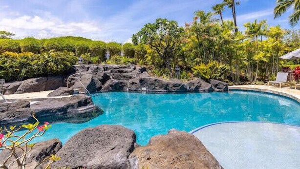 Ein Pool mit klarem, blauem Wasser, umgeben von Felsen und tropischer Vegetation.