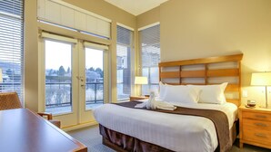 Quarto de hotel com uma cama grande, uma escrivaninha de madeira e vista através das portas de vidro.