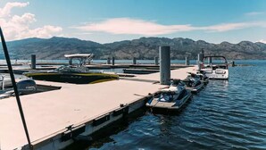 Uma marina com barcos atracados, céu claro e montanhas ao fundo.