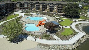Resort com vários edifícios, área de piscina central com escorrega e jardim ajardinado.