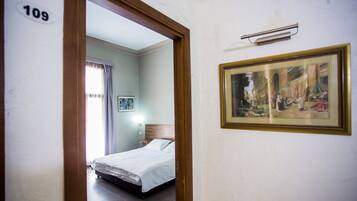 Quarto de hotel com uma cama, um quadro na parede e uma porta com o número 109.