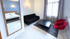 A hotel room with a bed, a black sofa, a coffee table, a red chair, and a large mirror. - Hotel Olympic (Fes)