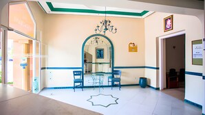 A hotel lobby with a reception desk, a chandelier, a mirror, and a star-shaped rug. - Hotel Olympic (Fes)