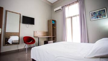 Habitación de hotel con cama, televisor, escritorio, una silla roja, armario y un cuadro.