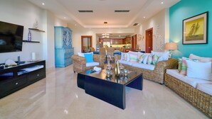 A spacious living room with a modern design, featuring a large black coffee table, wicker sofas, and a television on a black stand.