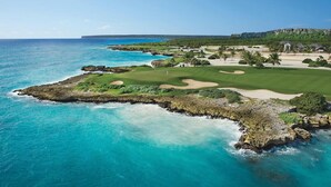 A coastal golf course with a clear view of the ocean and a distant mountain range.