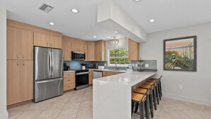 A modern kitchen with stainless steel appliances, wooden cabinets, and a large island with bar stools. - Single Level Home- 1 Minute Walk to the Beach- 5 minute walk to Restaurant/Shops (Holmes Beach)