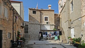 Eine enge Gasse mit Steinbauten, einem kleinen Tisch mit Stühlen und Wäsche, die an einer Leine aufgehängt ist.