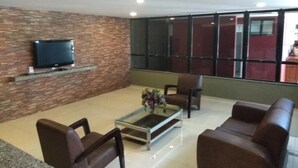 A lobby with a television mounted on a brick wall, a glass coffee table with flowers, and brown leather sofas. - Excellent fit 2 bedrooms fully furnished, cable TV, sea view from the balcony (CE)