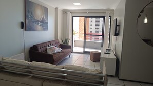 A modern living room with a brown sofa, a small table, a TV, and a balcony with a view of buildings. - Excellent fit 2 bedrooms fully furnished, cable TV, sea view from the balcony (CE)