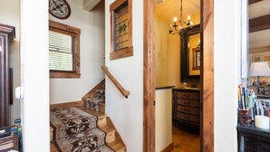 A staircase with patterned carpet steps leading to a room with wooden beams, a chandelier, and a cabinet with drawers. - Stunning Lake Views with private boathouse deck, hot tub and close walk to town (Grand Lake)