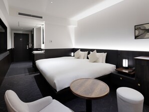 Une chambre d’hôtel moderne avec un grand lit, des tables de chevet, une table ronde en bois, une chaise et un petit tapis rond.