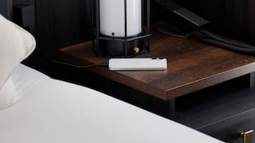 A neatly made bed with a white pillow, a bedside table with a white phone, a black lamp, and a black telephone.
