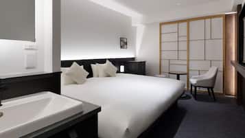 A modern hotel room with a large bed, a bedside table, a chair, a small table, and a TV.