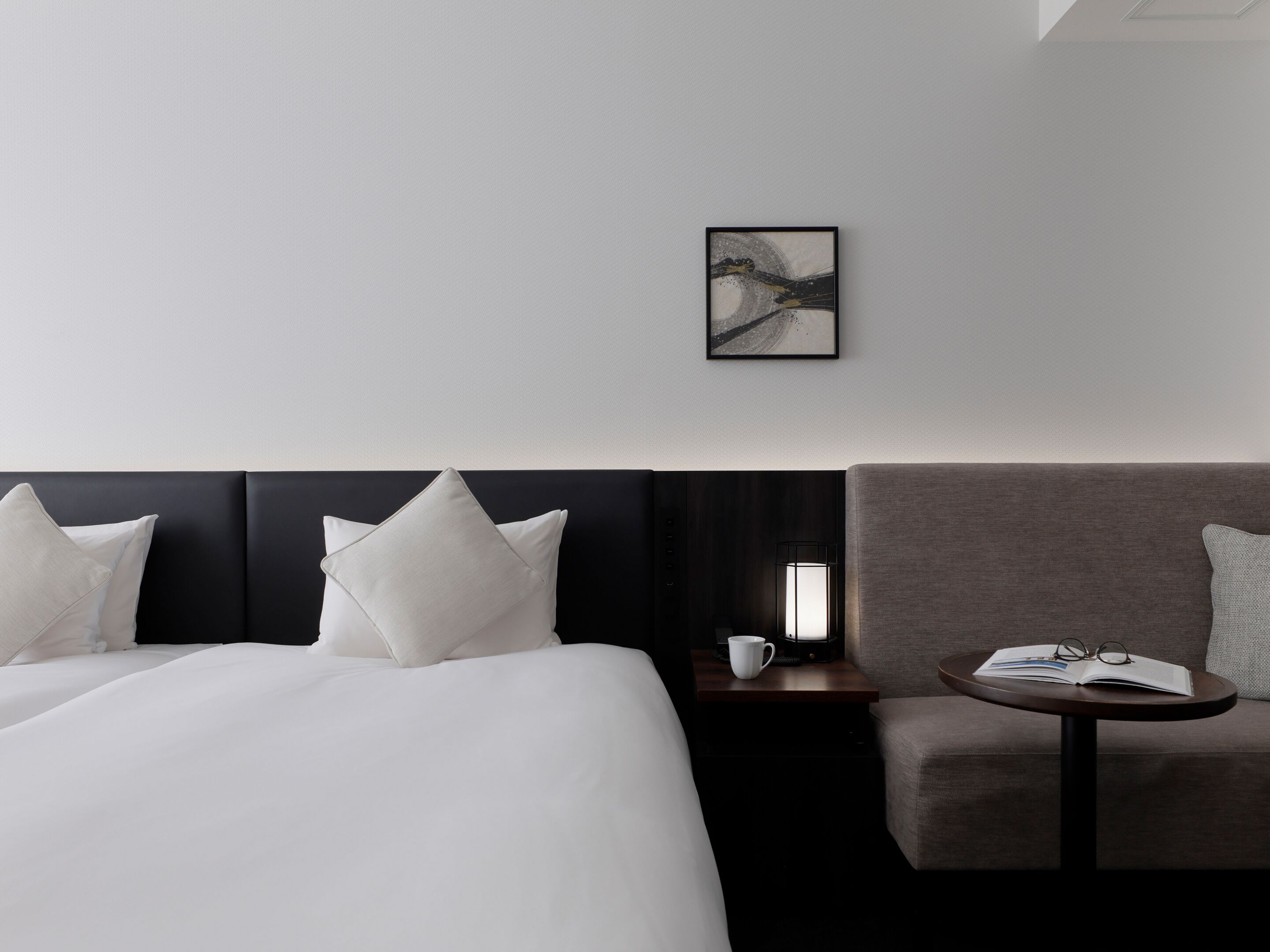 Habitación de hotel con cama, sofá, mesita de noche con lámpara y un cuadro en la pared.