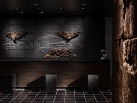 A modern interior with dark wood paneling, a tiled floor, and a central decorative wall with relief sculptures.