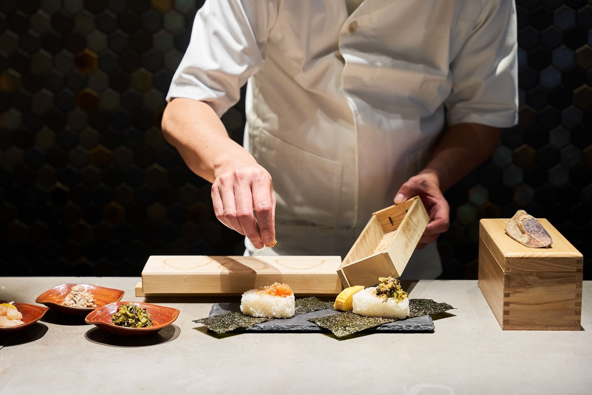 A chef preparing sushi with wooden boxes and plates on a table.