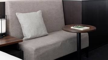 A modern room with a grey sofa, a round wooden side table, and a pair of glasses on the table.