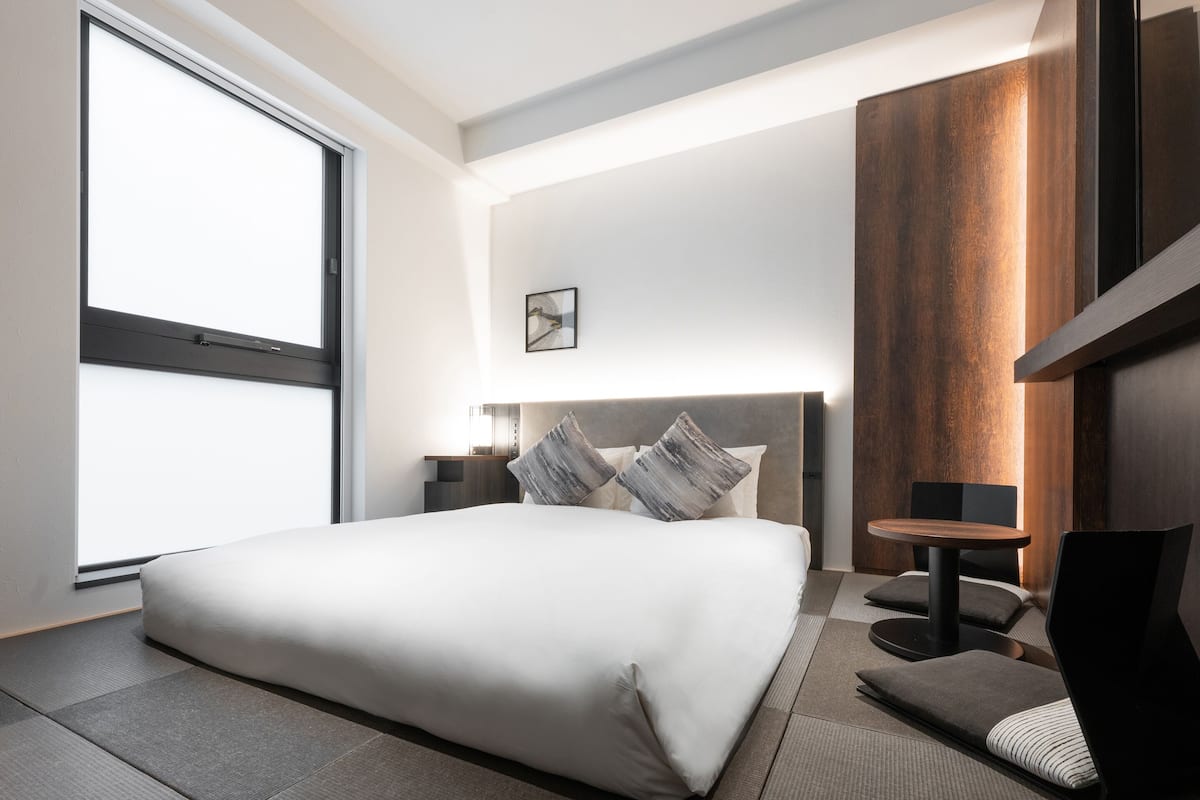 Et moderne hotelværelse med en stor seng, et sengebord, en stol, et lille bord og et stort vindue.