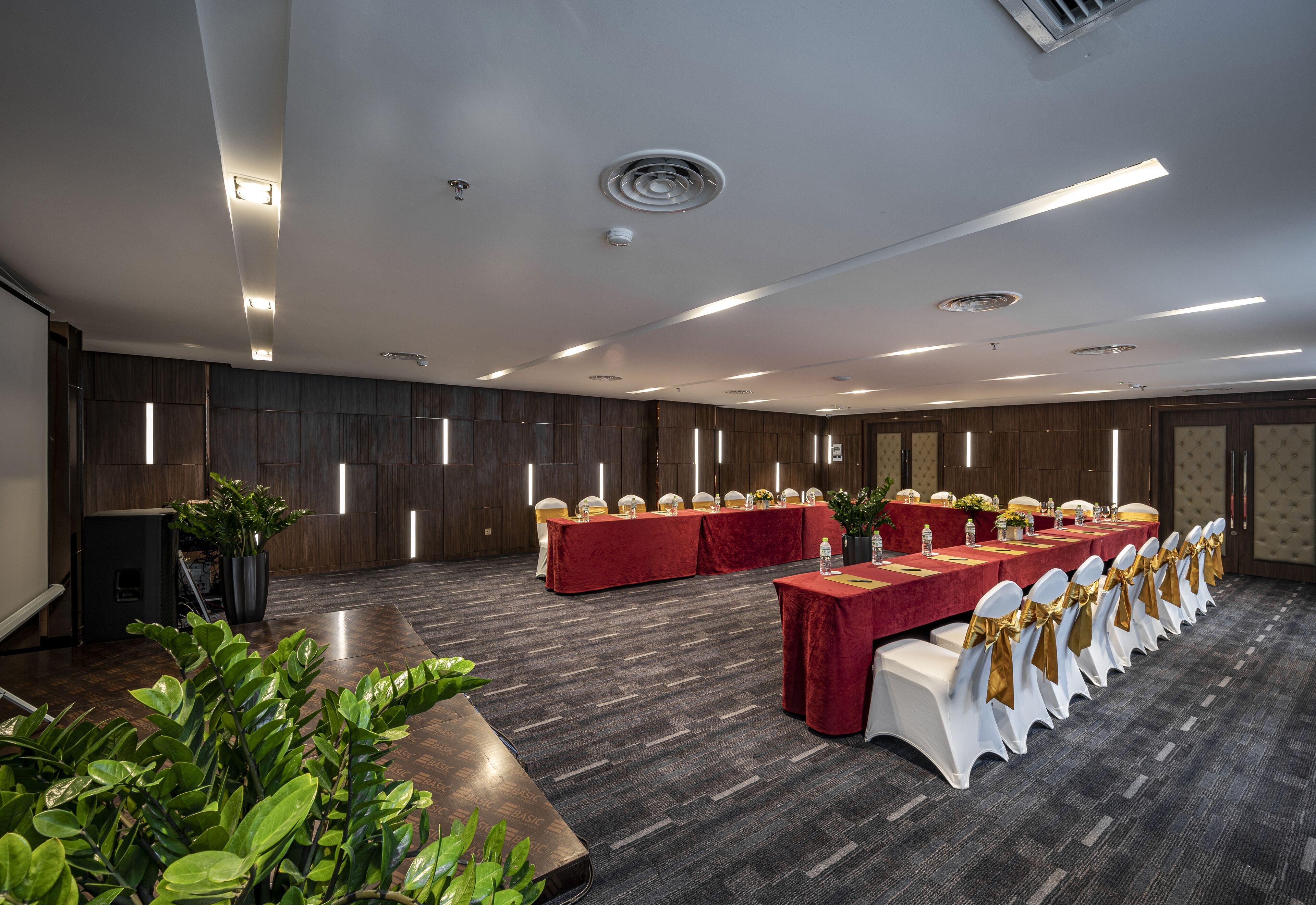 A conference room with a long table, white chairs with gold sashes, and a red tablecloth.