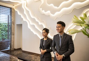 Two individuals in business attire standing in a modern lobby with a unique light design on the wall and a plant in the foreground. - Muong Thanh Luxury Saigon Hotel (Ho Chi Minh City)