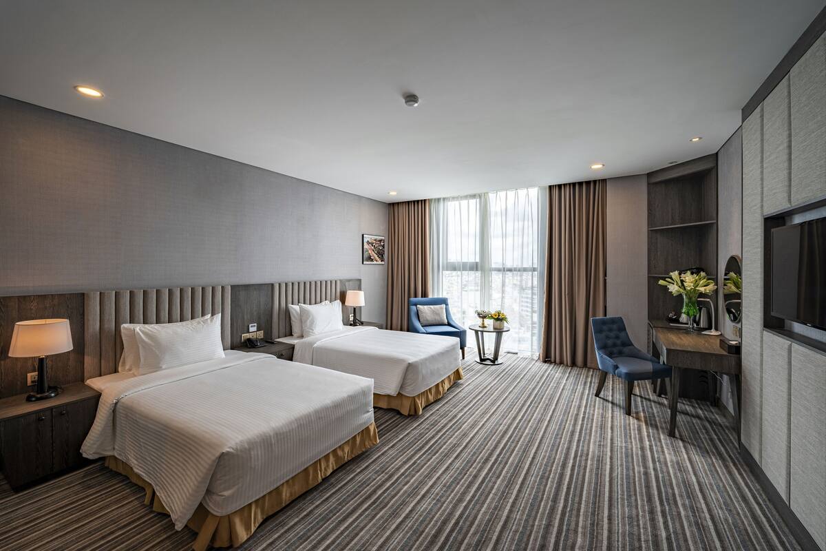 A hotel room with two beds, a desk, a chair, a TV, and a window with curtains.