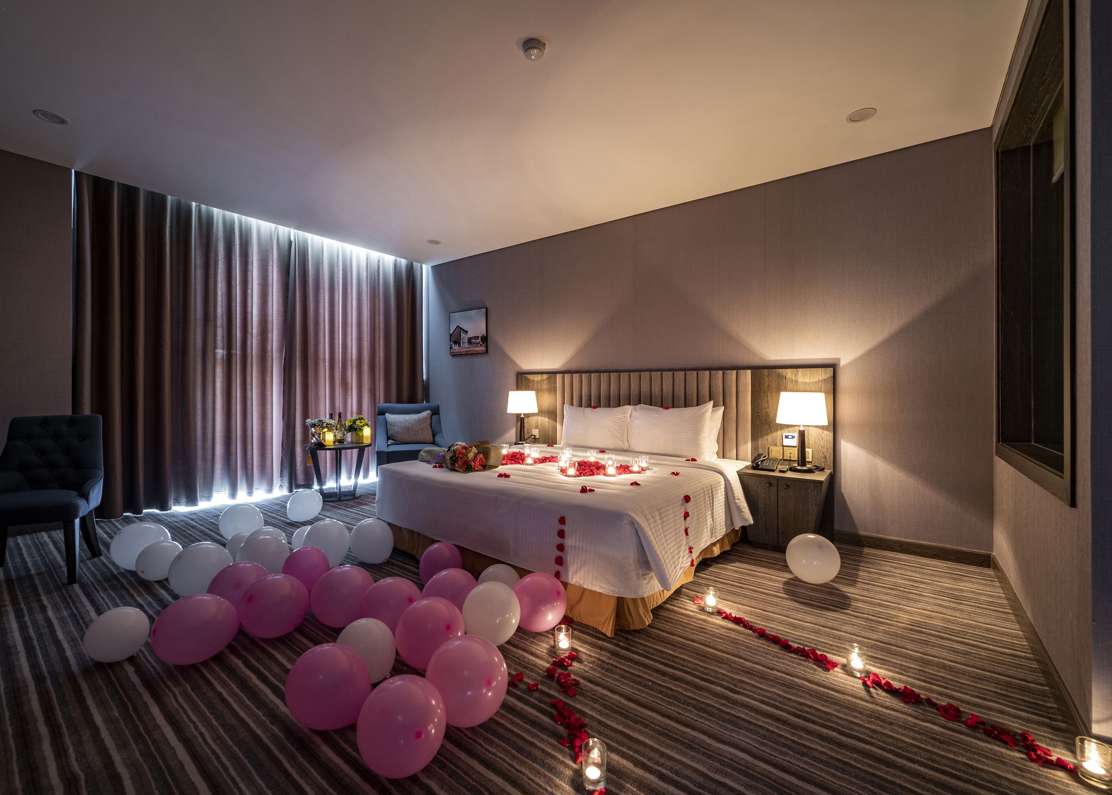A hotel room with a bed, bedside tables, a chair, and a large window with curtains.