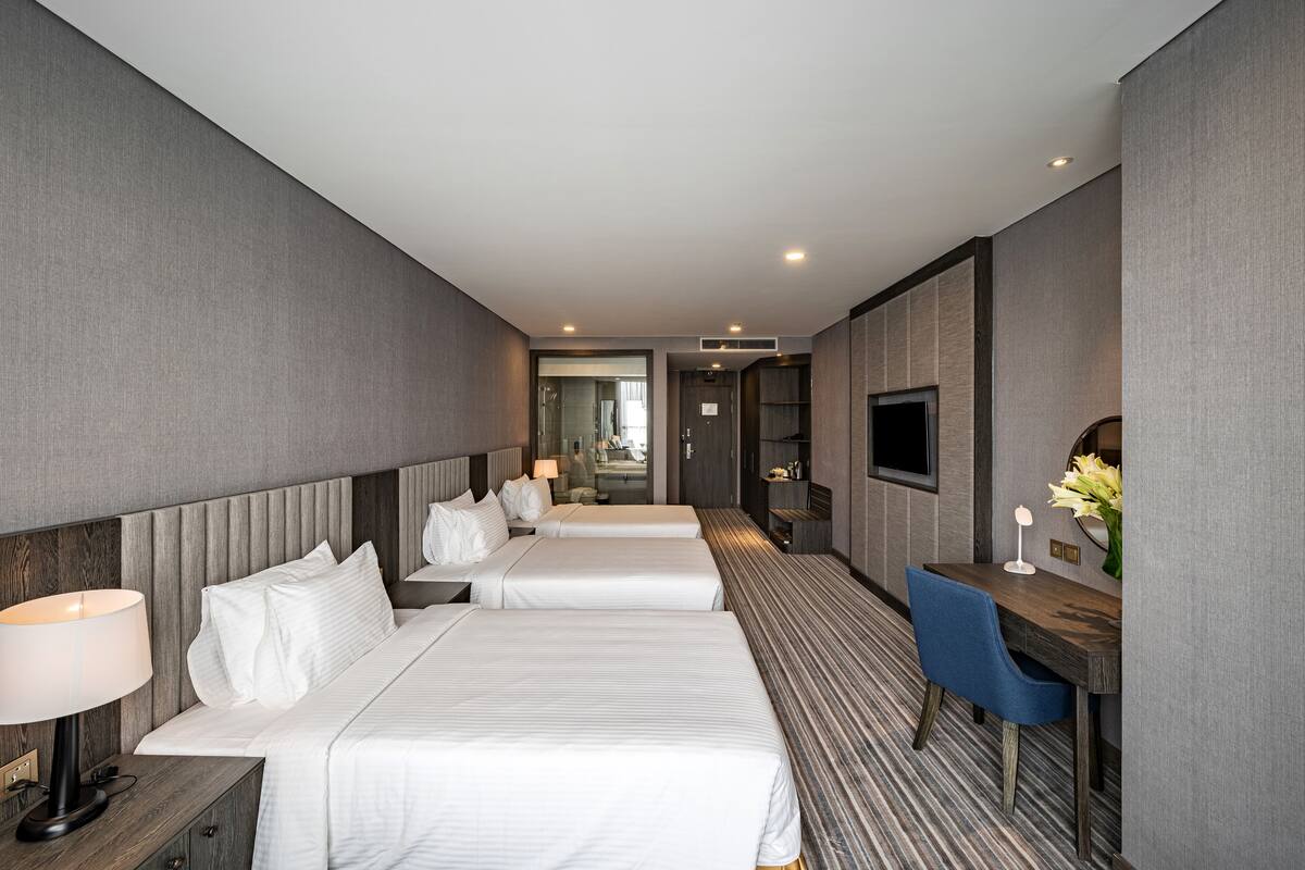 A hotel room with two beds, a desk, a chair, a TV, and a mirror.