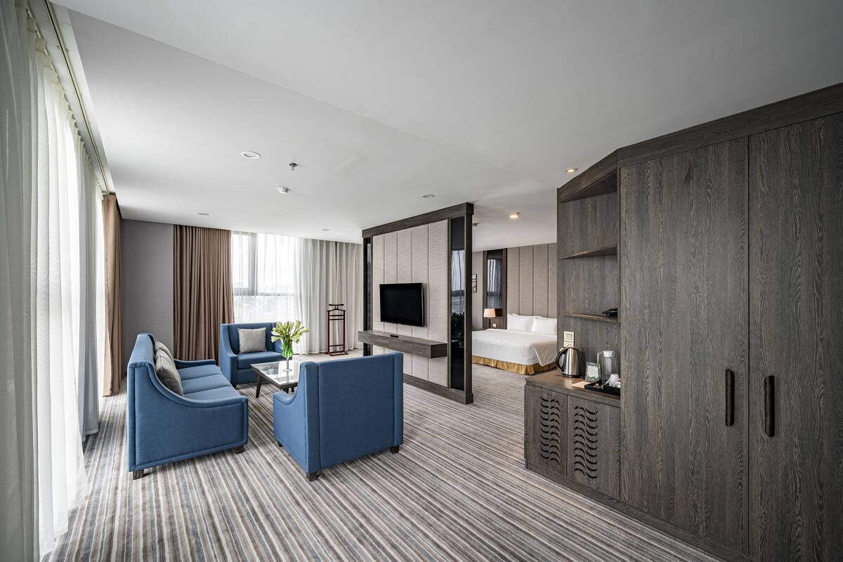 A modern hotel room with a large bed, a TV, a sofa, and a cabinet.