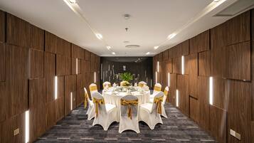 A conference room with a round table, white chairs with gold sashes, and a dark carpeted floor.