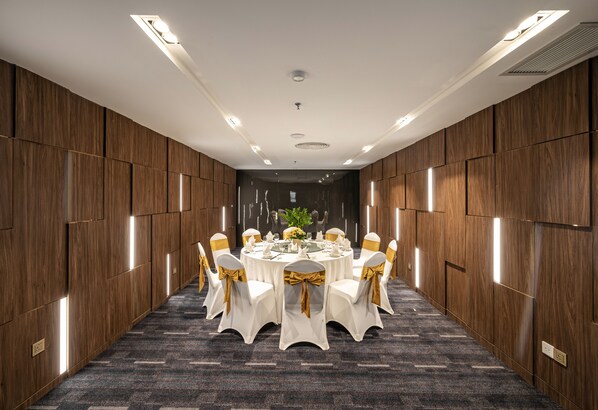 A conference room with a round table, white chairs with gold sashes, and a dark carpeted floor.