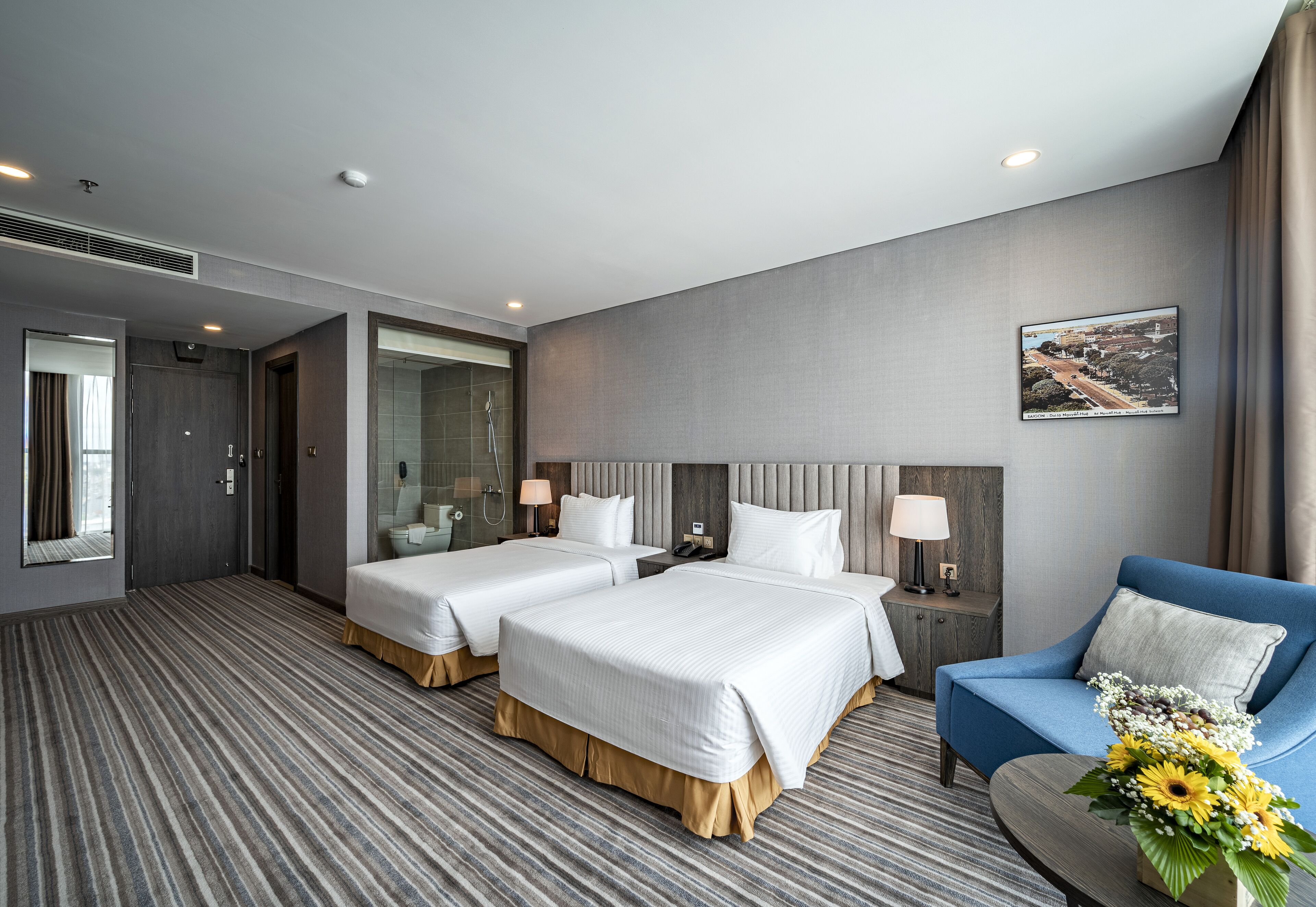 Habitación de hotel con dos camas, ducha, zona de estar y vistas a un paisaje urbano.