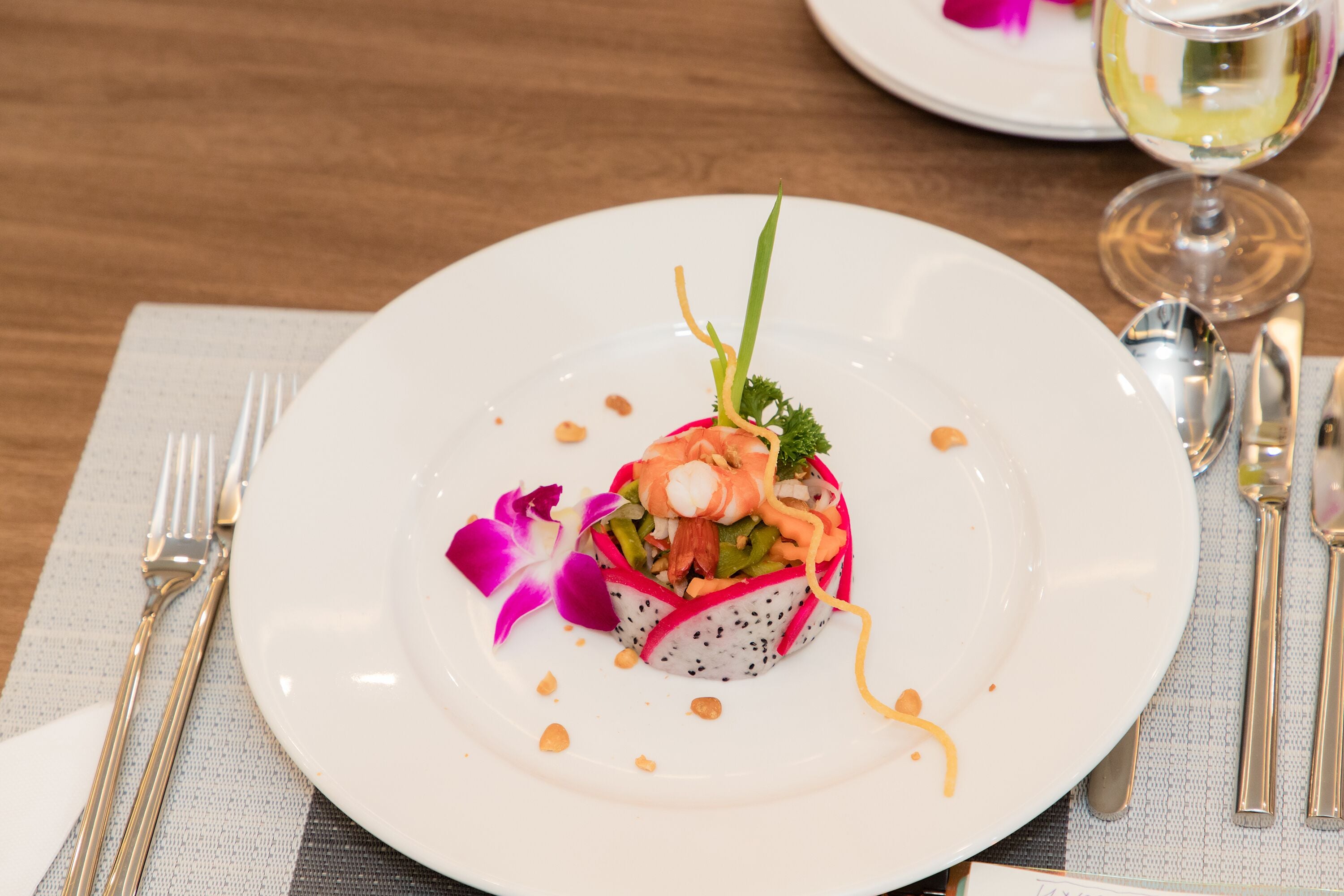 A white plate with a seafood dish, garnished with a purple flower, on a table with a placemat.