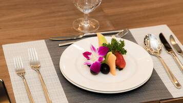 A neatly arranged dining table with a white plate of fruit, a glass of water, and a wine glass.