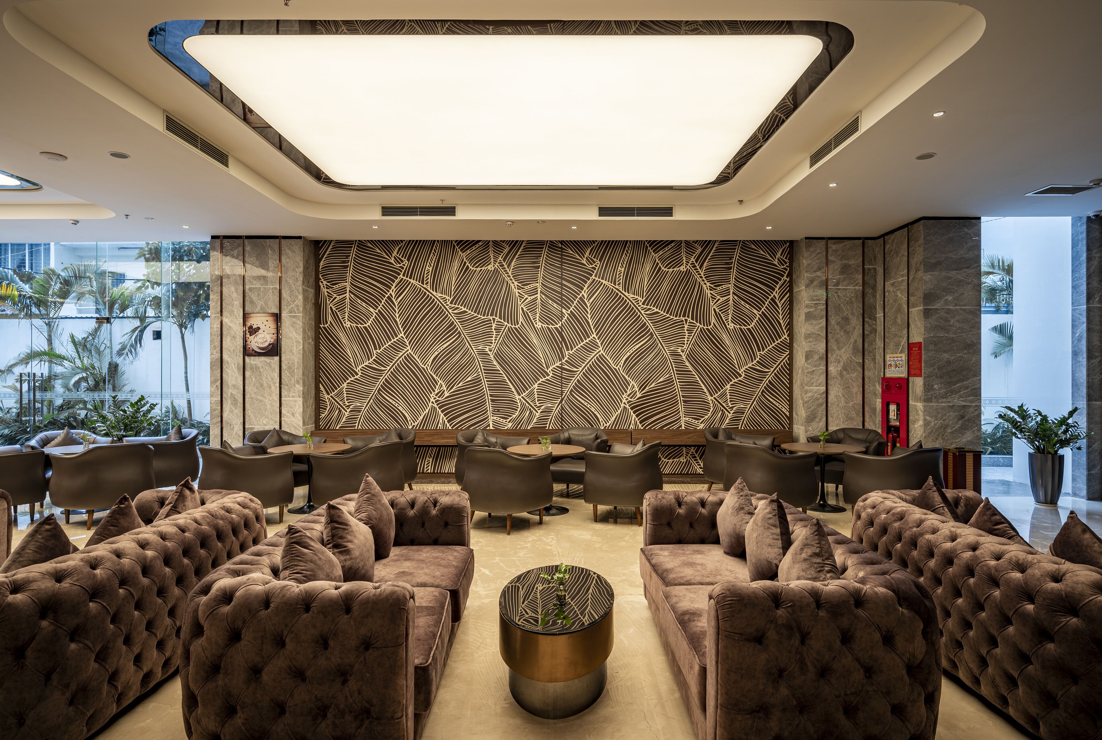 Un salon moderne avec des canapés capitonnés, une table basse centrale et un mur orné d’un motif décoratif.
