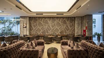 Un salon moderne avec des canapés capitonnés, une table basse centrale et un mur orné d’un motif décoratif.