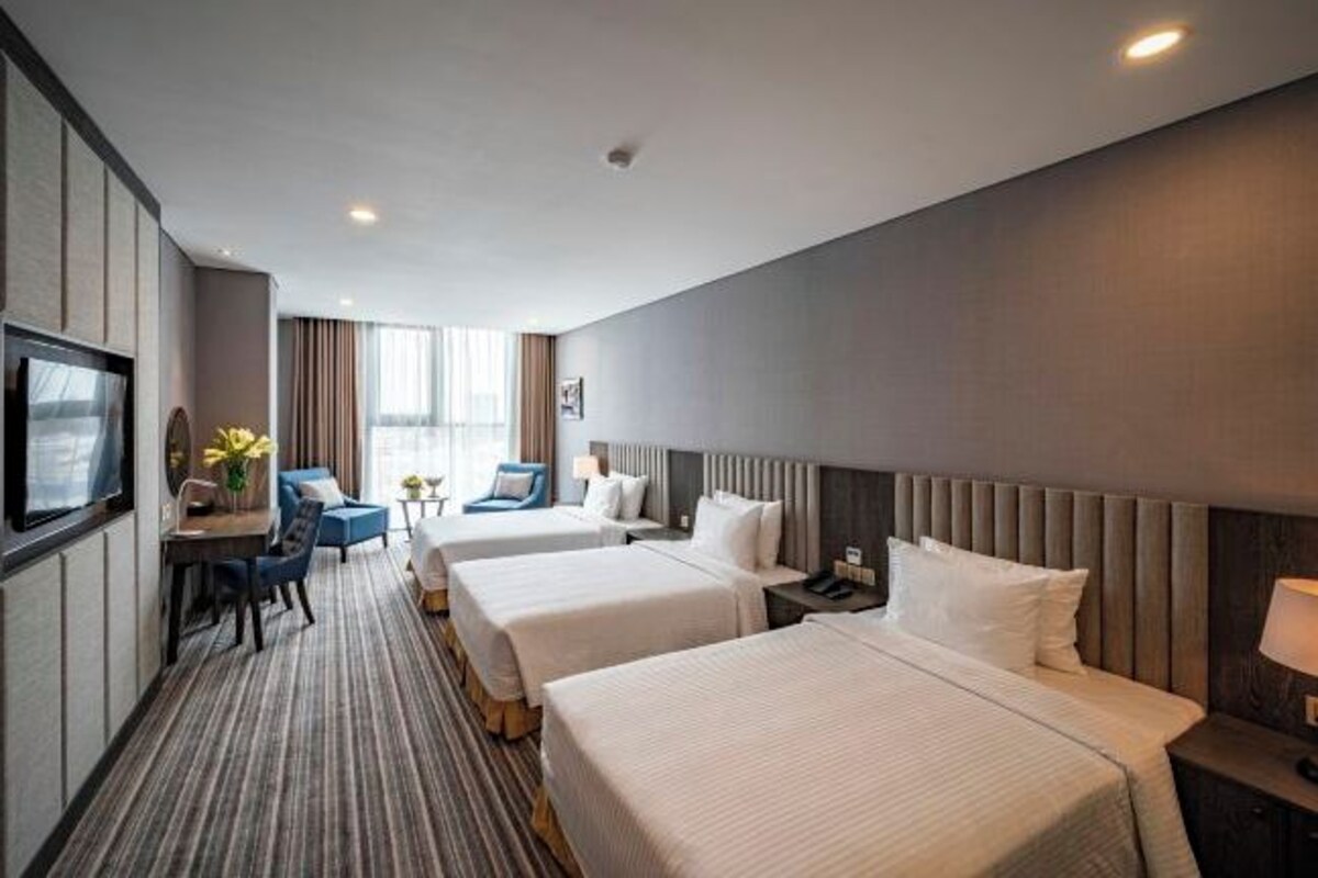 A hotel room with two beds, a desk with a chair, a TV, and a window with curtains.