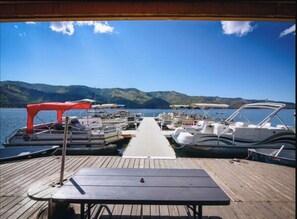 A dock with several boats, a table, and a view of a lake with hills in the background.