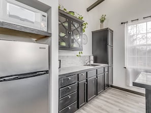 A modern kitchen with a built-in microwave, stainless steel refrigerator, dark wooden cabinets, and a window with sheer curtains.