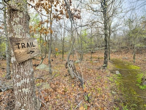 A wooden trail sign in a forested area with a path leading through the woods.