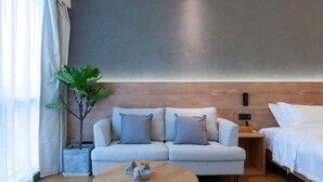 Une chambre d’hôtel moderne avec un canapé, un lit, une petite table et une plante.