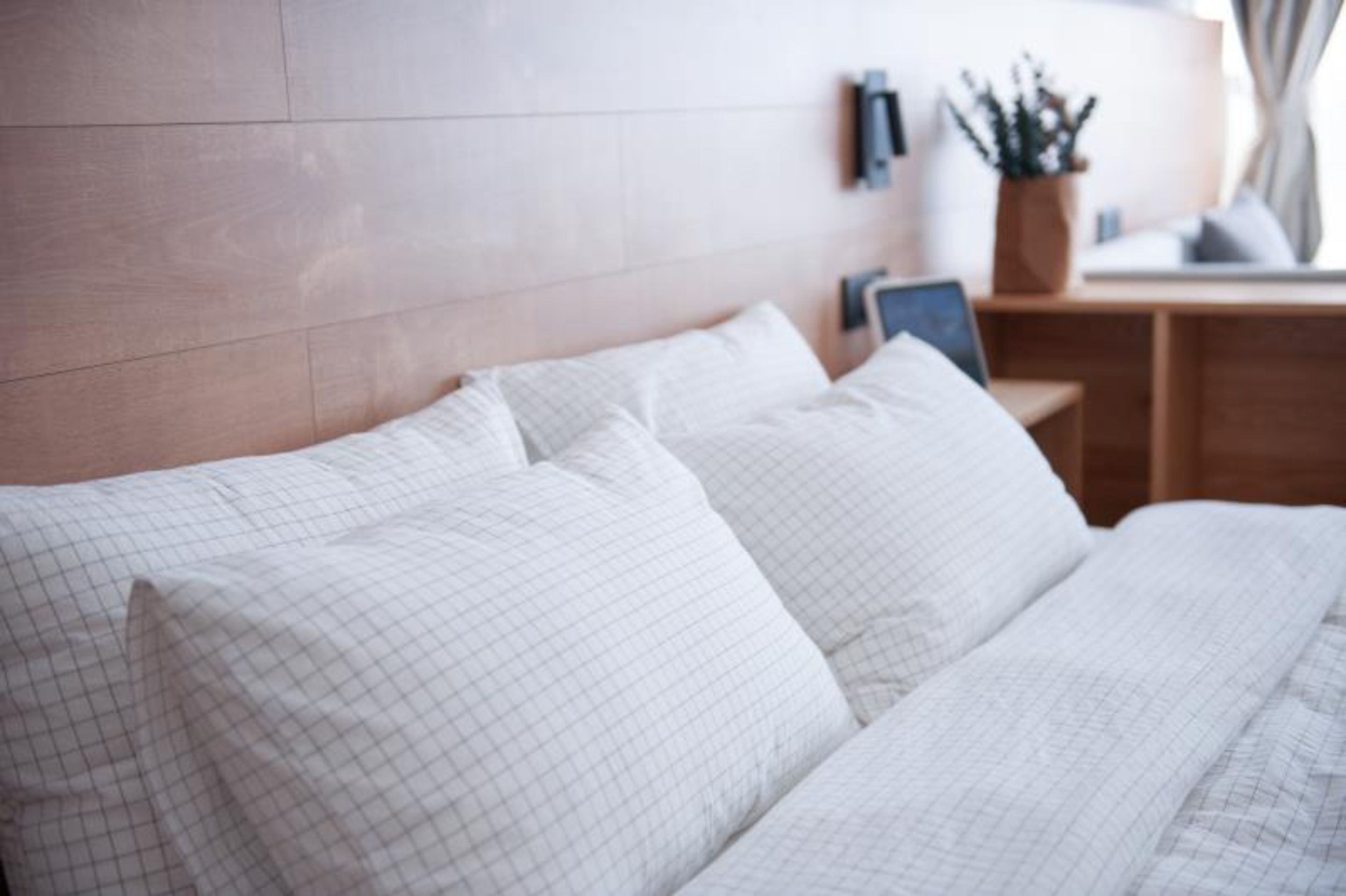 A neatly made bed with white linens and a wooden headboard.
