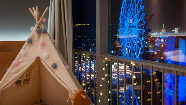 Une pièce avec vue sur le paysage urbain et une grande roue, un plancher en bois et une décoration évoquant une tente.