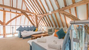 A spacious room with a high ceiling and exposed wooden beams, featuring a bed, a sofa, and a small table with a lamp. - Great Higham Barn Complex by Bloom Stays -  sleeps 44 in 13 bedrooms (Sittingbourne)