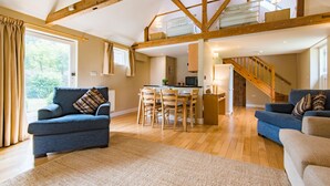 A spacious living area with a high ceiling and exposed wooden beams, a dining area with a table and chairs, and a staircase leading to an upper level. - Great Higham Barn Complex by Bloom Stays -  sleeps 44 in 13 bedrooms (Sittingbourne)