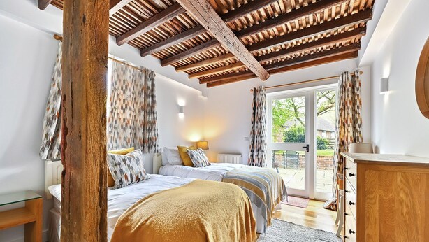 A bedroom with a wooden ceiling, a large bed with multiple pillows, a bedside table, and a view of the outdoors through a glass door.